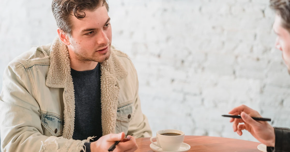 Deux collègues en entretien individuel à une table en bois clair, carnet ouvert et stylo, lors d'un point d'accompagnement professionnel.