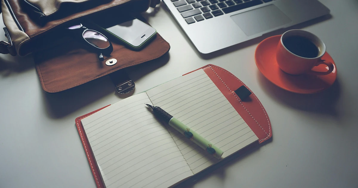 Entrepreneur notant son plan éditorial LinkedIn dans un carnet, téléphone avec notifications réseaux sociaux, lumière matinale naturelle.