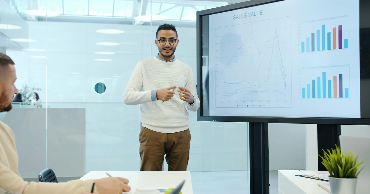 Expert PowerPoint accompagnant un professionnel sur double écran dans un bureau moderne